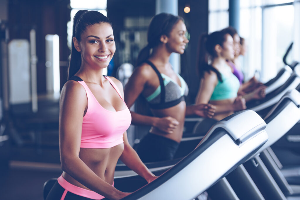 Woman in athletic clothing smiling while walking on a treadmill to prevent vein disease.